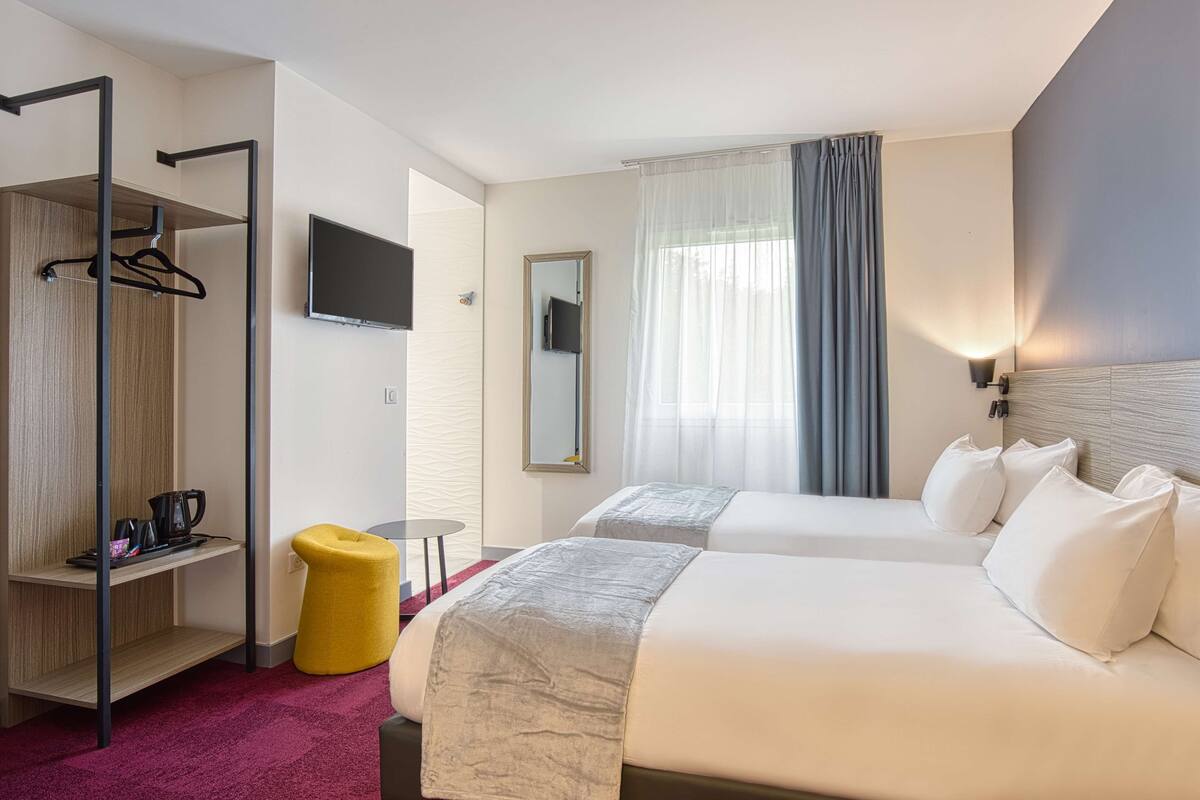 Une chambre d’hôtel avec deux lits, une télévision, un miroir, une armoire et une petite table.
