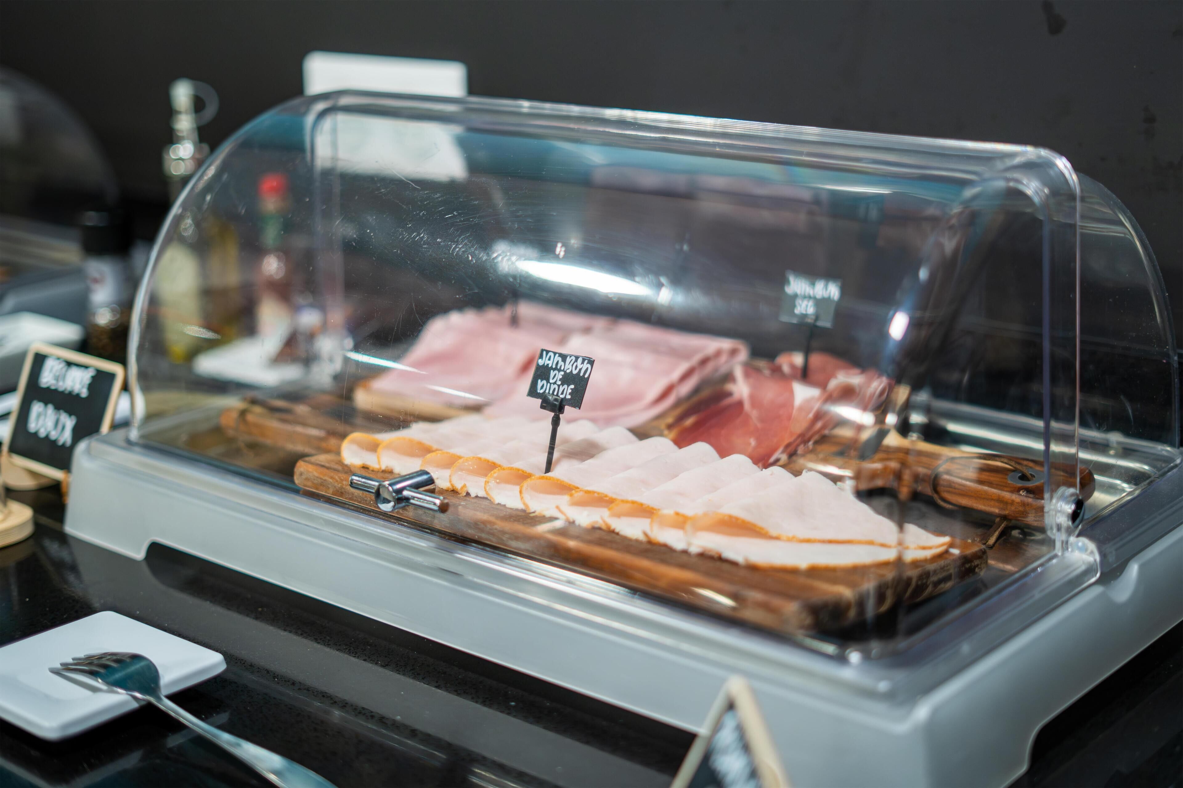 A glass display case with various meats, including ham and bacon, and a sign indicating 'Jambon de Vie'.