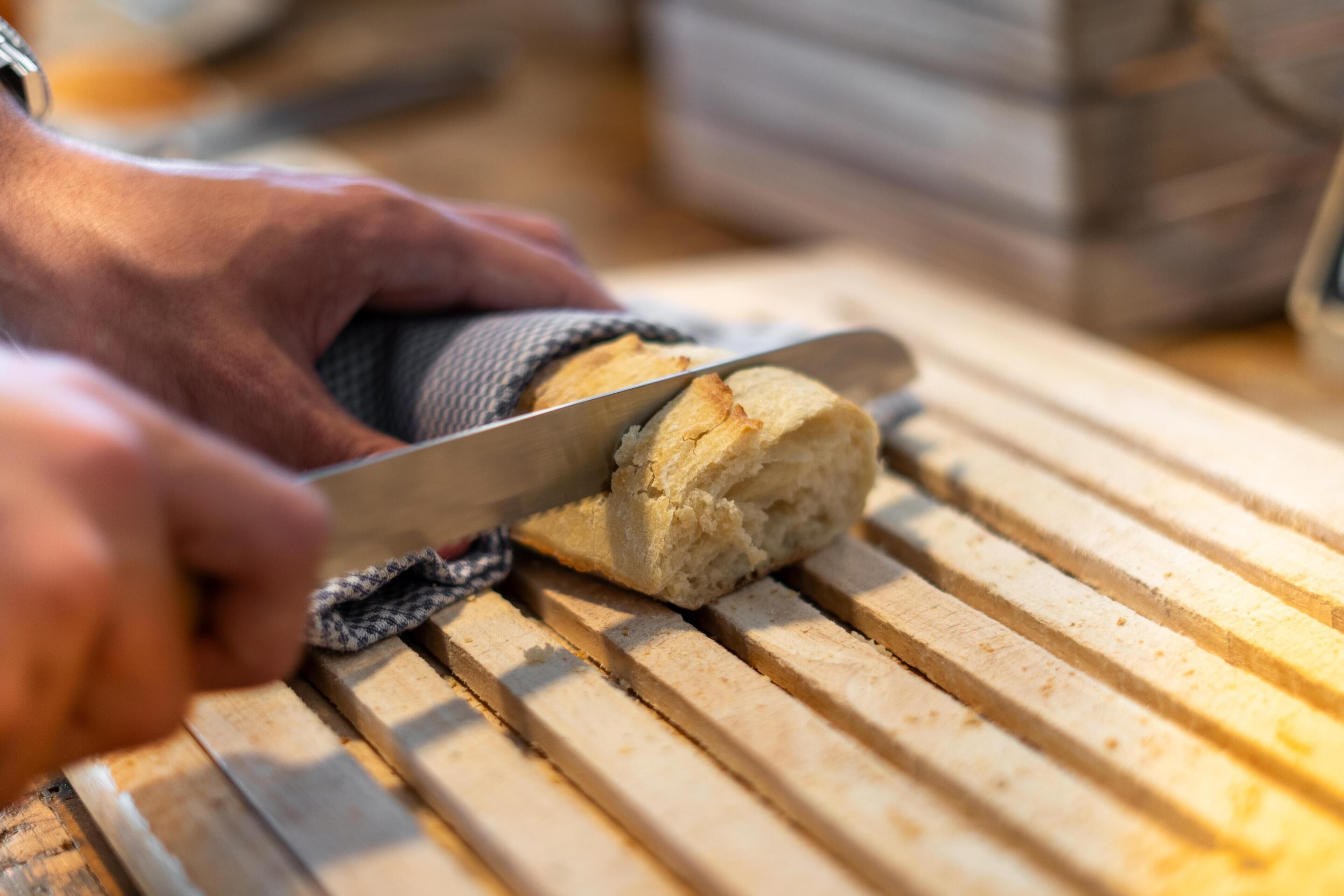 A hand cutting a loaf of bread on a wooden cutting board.