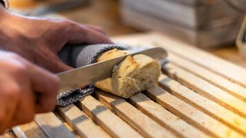 A hand cutting a loaf of bread on a wooden cutting board.