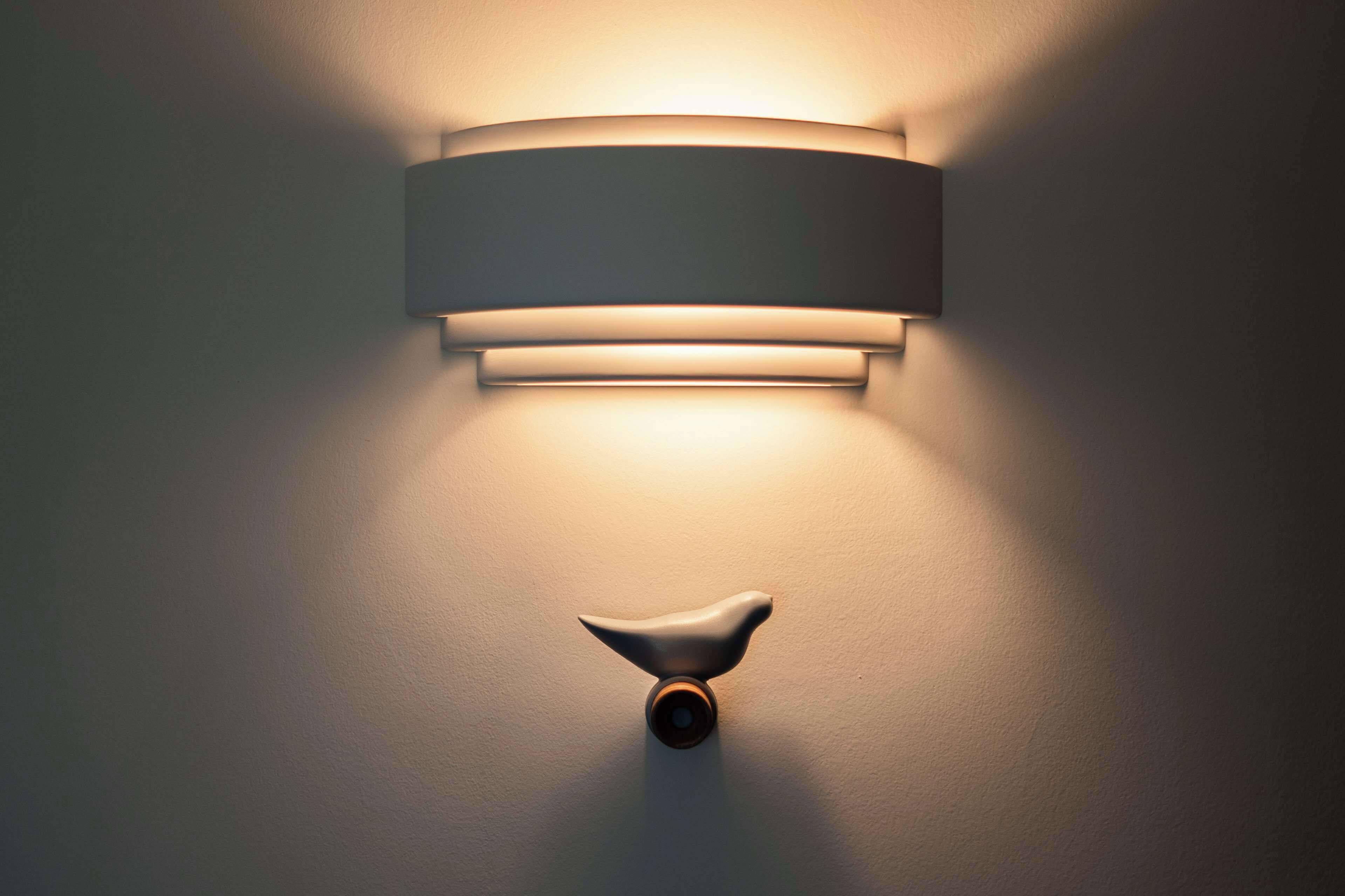 A wall-mounted light fixture with a cylindrical shade and a bird-shaped accent.