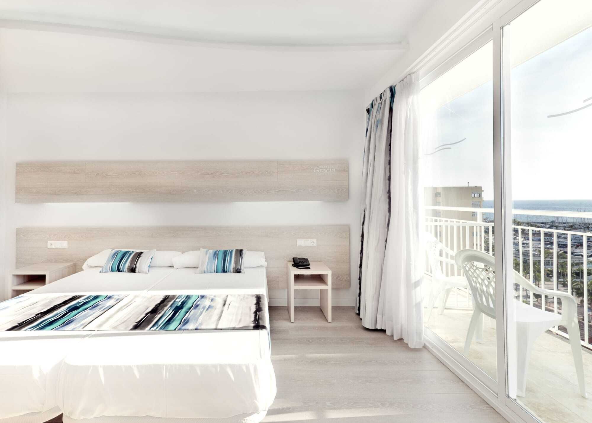 Una habitación de hotel con una cama grande, una mesita de noche, una silla y un balcón con vistas a la ciudad.
