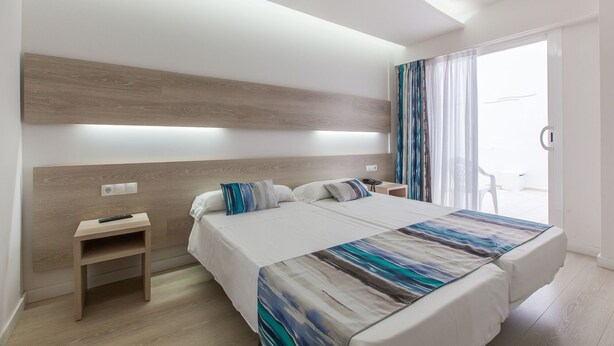 Quarto de hotel moderno com uma cama grande, mesas de cabeceira e vista para o exterior.