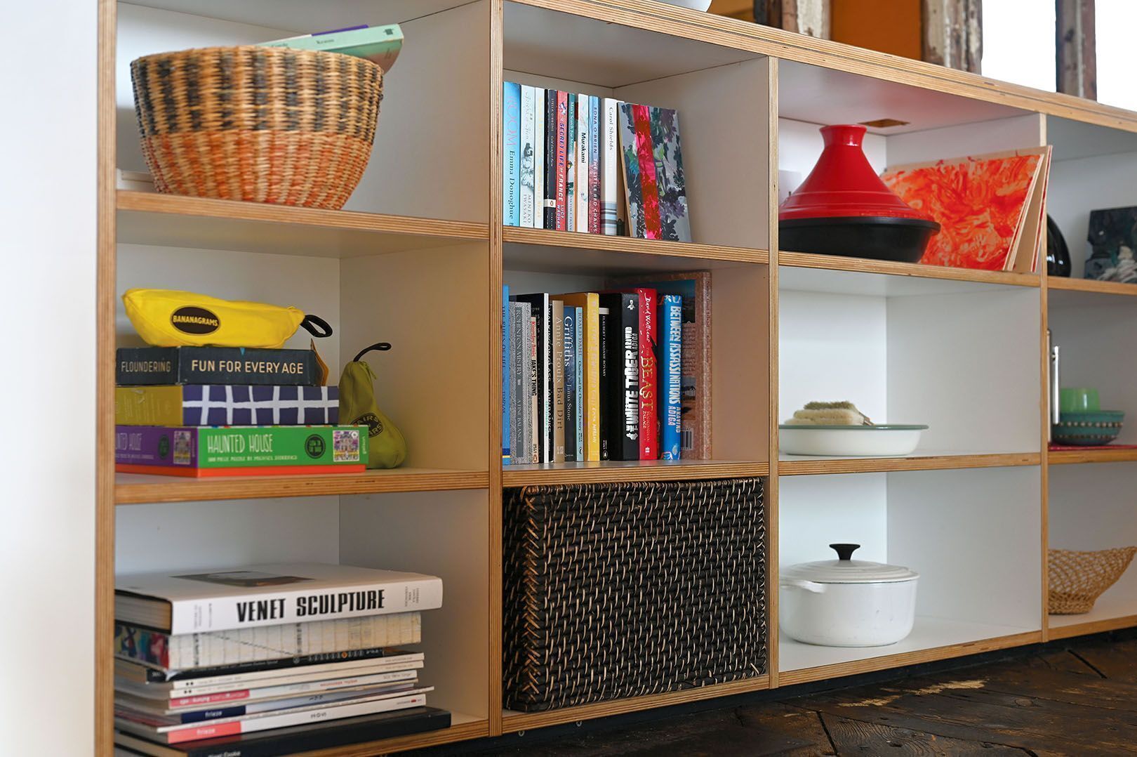 Une bibliothèque remplie de divers livres, un panier en osier et une lampe rouge.