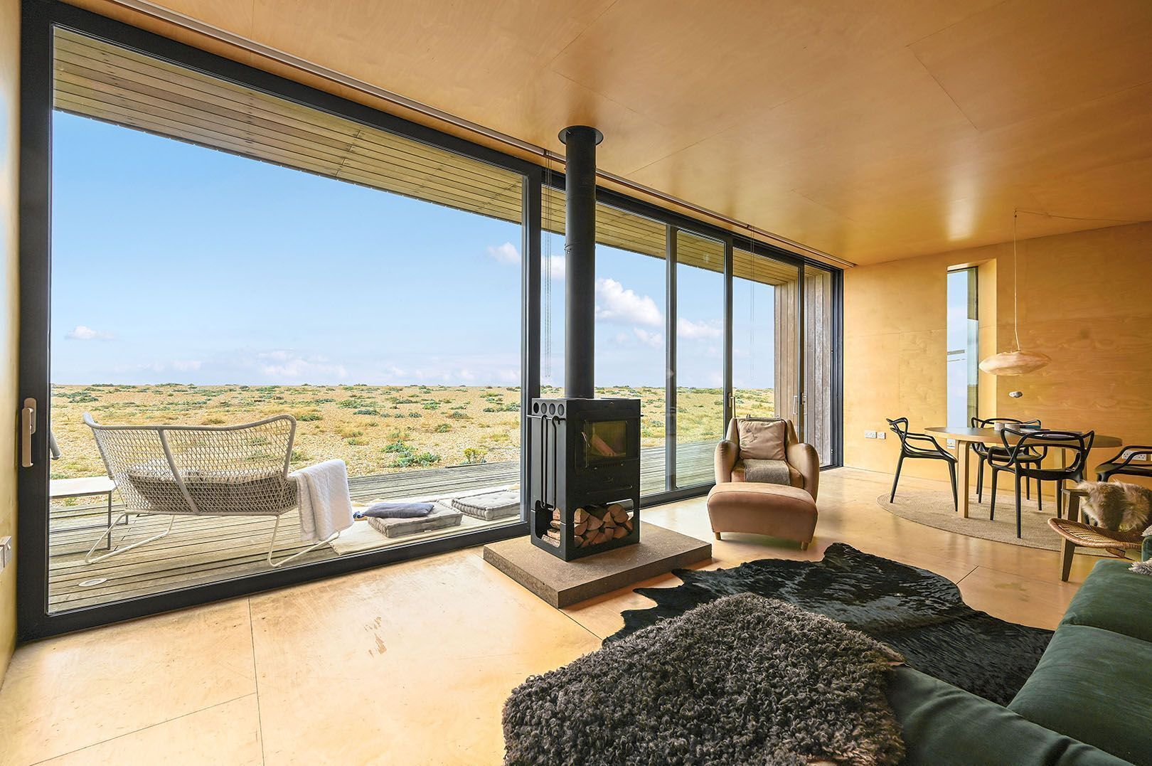 A modern living room with a large glass door leading to an outdoor area, a fireplace, and a dining set.