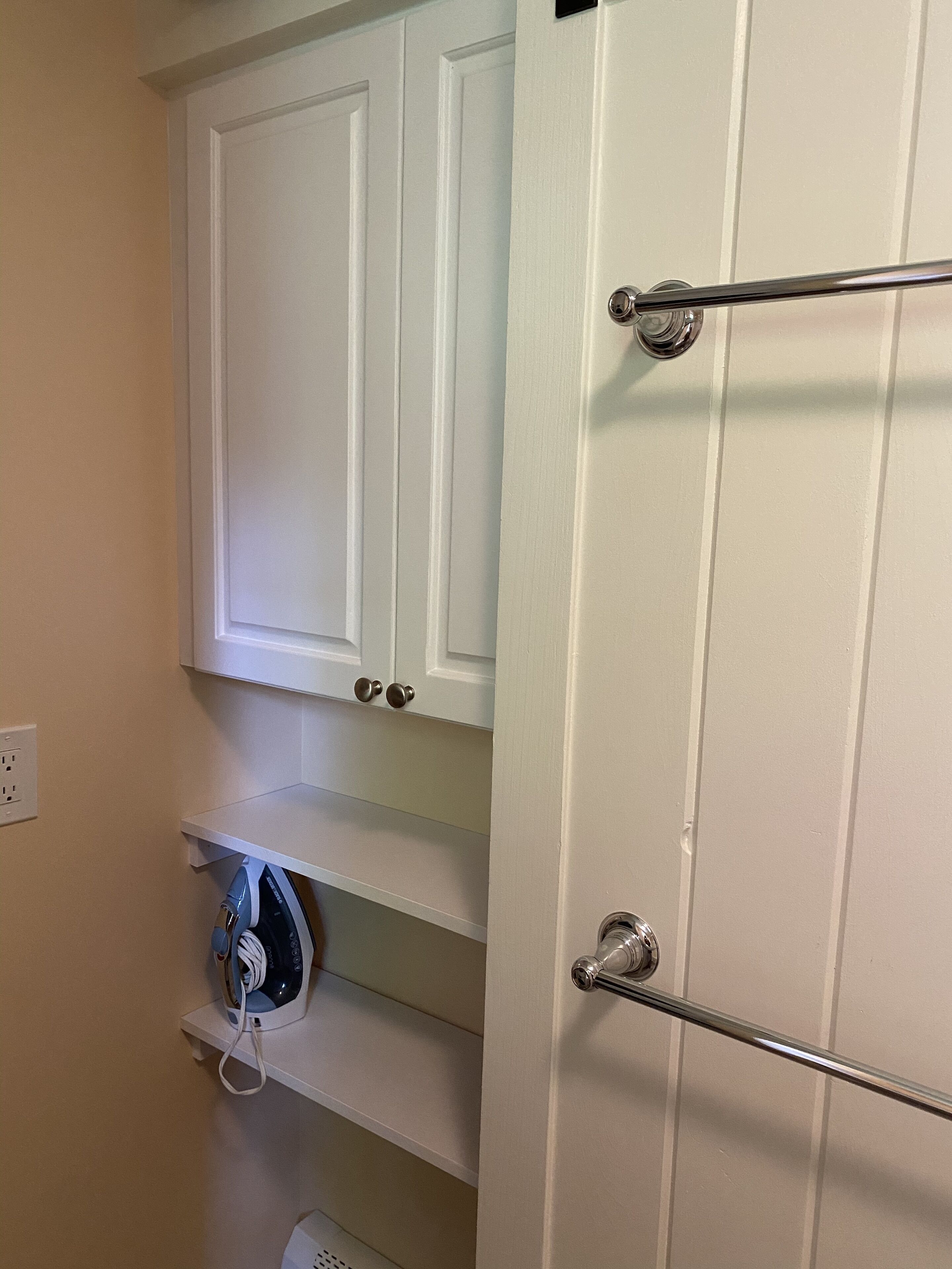 A bathroom with a white door, a towel rack, and a shelf with a hairdryer.