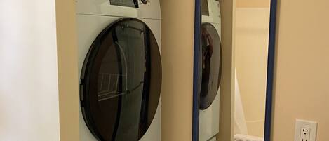 A laundry room with stacked washers and dryers, a mirror, and a toilet visible in the reflection.