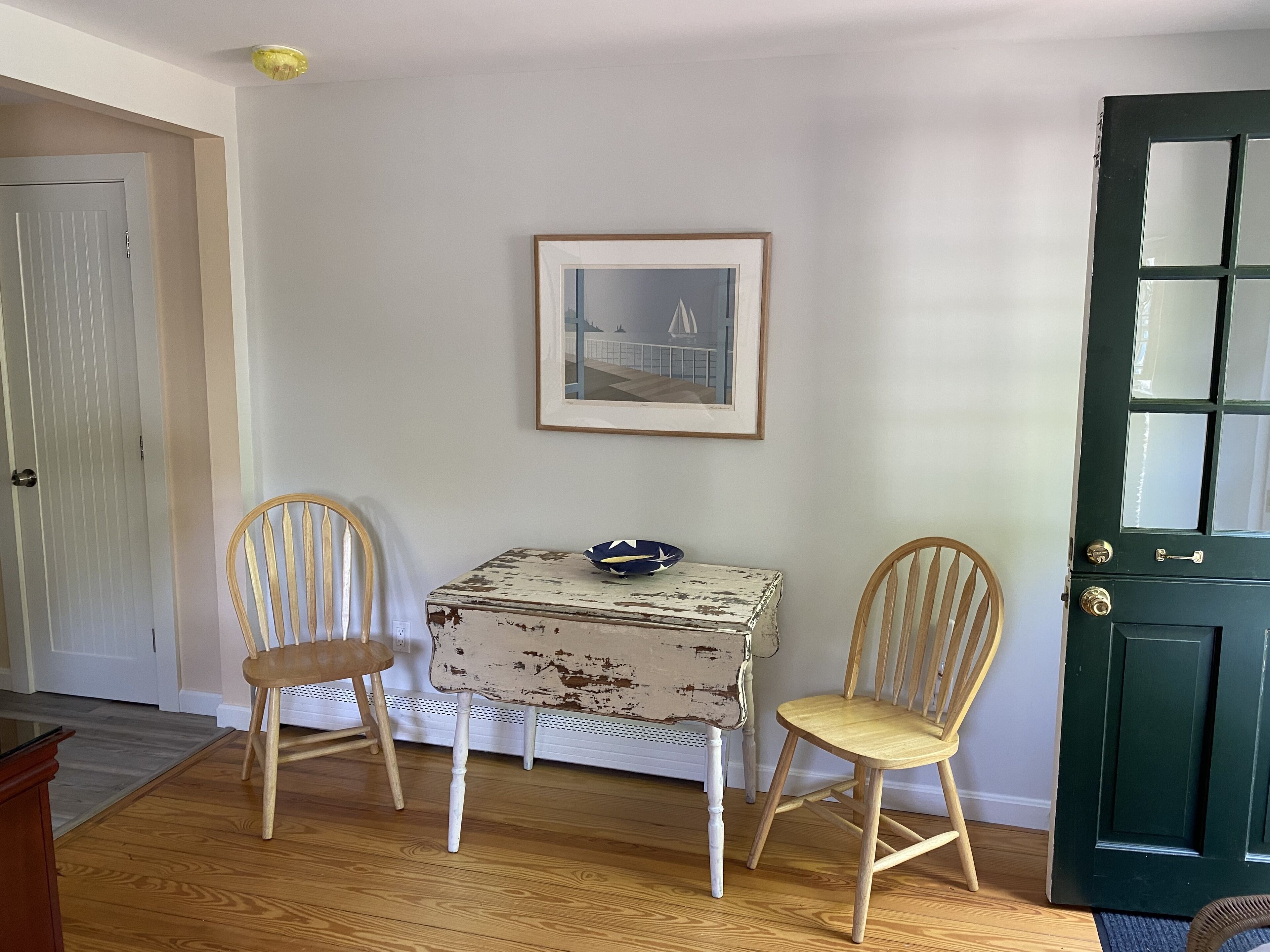 A room with a wooden floor, a white door, a green door, and two wooden chairs.