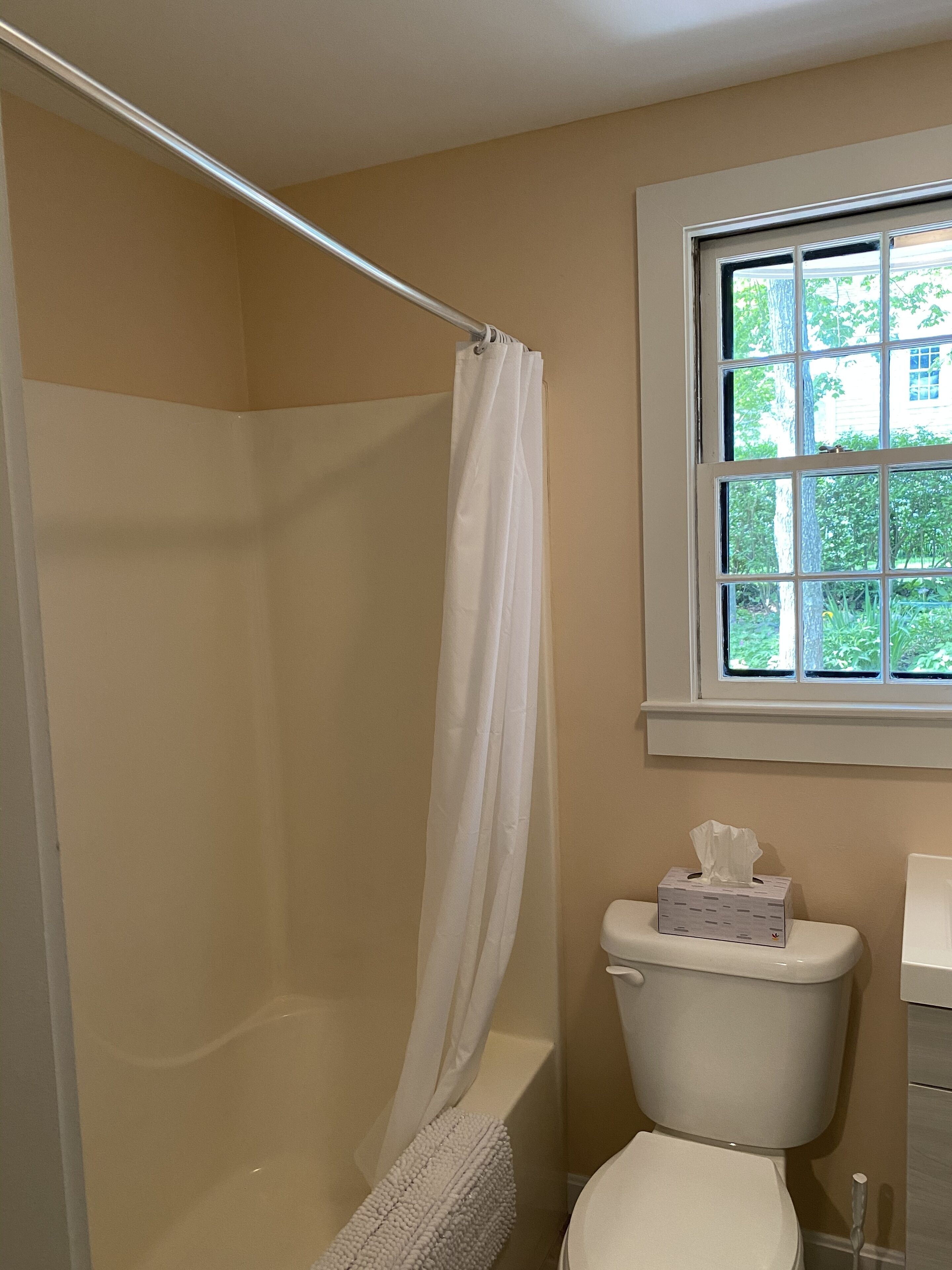 A bathroom with a shower, toilet, and window.