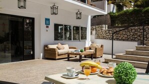 An outdoor seating area with wicker furniture, a table with breakfast items, and a stone wall. - Marigna (Ibiza Town)