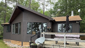 A cabin with a deck, a satellite dish, and a chimney.