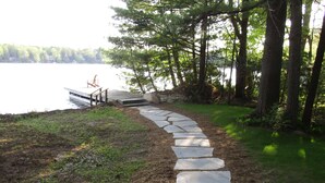 A stone pathway leading to a dock by a lake, surrounded by trees.