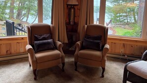 A cozy room with two armchairs facing a large window overlooking a forested area.