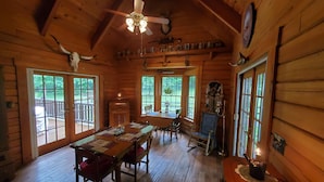 A wooden cabin interior with a dining table, chairs, a fireplace, and a ceiling fan. - Spring Acre Log Cabin (Paradise)