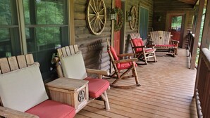 A wooden cabin with a porch featuring rocking chairs and a wooden bench. - Spring Acre Log Cabin (Paradise)