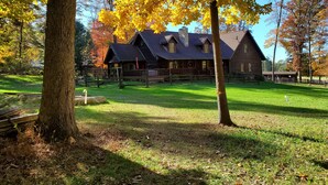 A rustic log cabin with a stone chimney, surrounded by a wooden fence and a grassy yard. - Spring Acre Log Cabin (Paradise)
