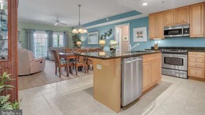 A spacious kitchen with a central island, wooden cabinets, stainless steel appliances, and a dining area with a cushioned chair and table. - Luxury Waterfront Condo  (Ocean City)