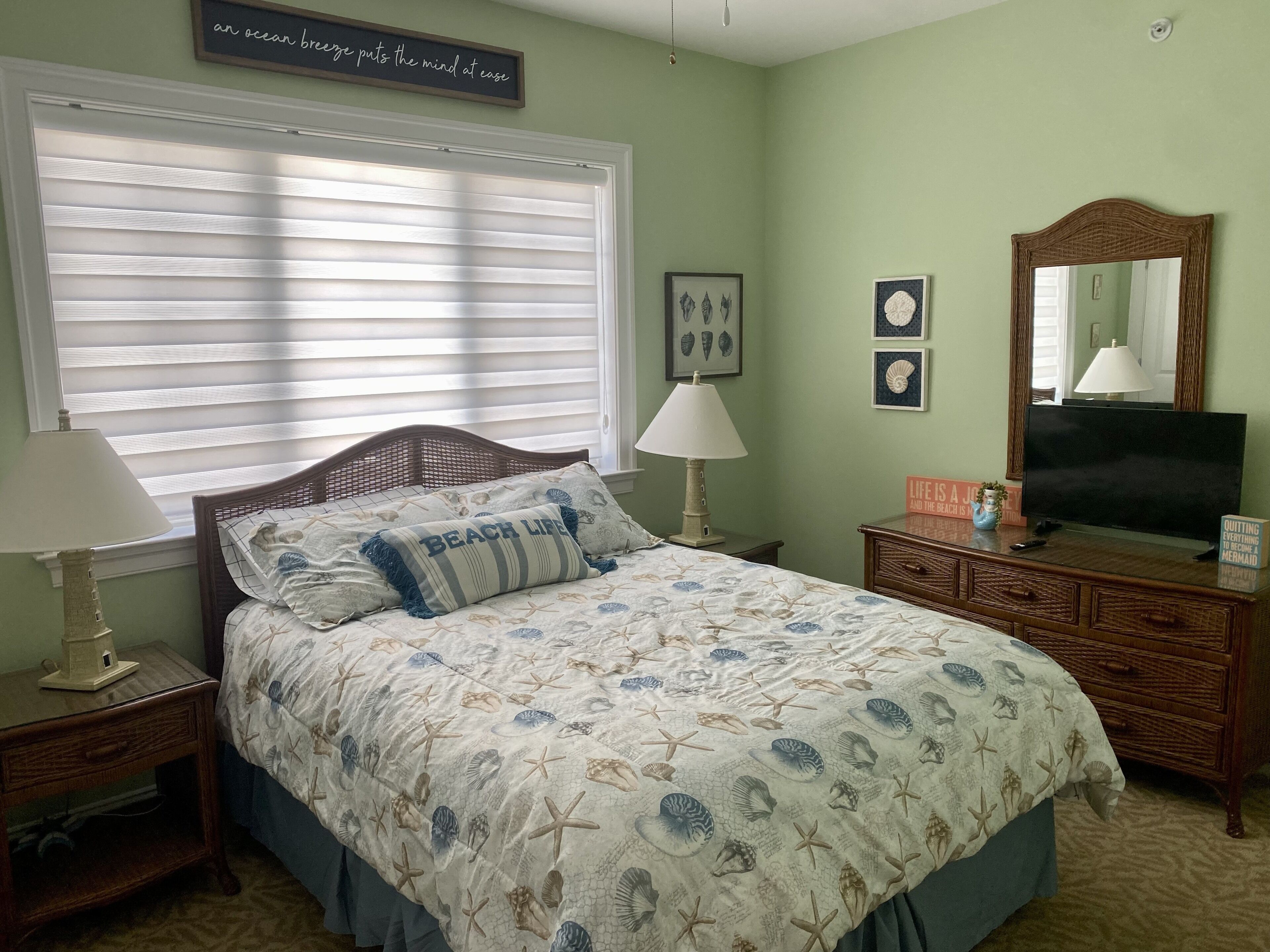 A bedroom with a bed, a nightstand, a dresser, a mirror, and a window with blinds.