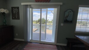 Ein Zimmer mit einer Schiebetür zu einer Terrasse, einem gerahmten Bild von einer Palme und einem Buch mit dem Titel 'The Blue Heron' an der Wand.