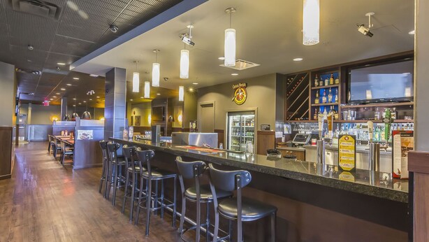 Una zona de bar con una barra larga, varios taburetes e iluminación colgante.
