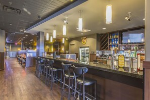 A bar area with a long counter, multiple stools, and overhead lighting. - Quality Inn and Suites Saskatoon (Saskatoon)