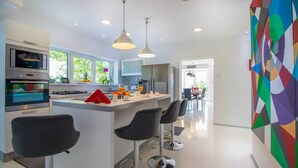 A modern kitchen with a central island, bar stools, and a dining area with a view. - Villa Evergreen with Pool (Crikvenica)