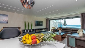 A modern living room with a large window, a dining area with fruit, and a sofa.