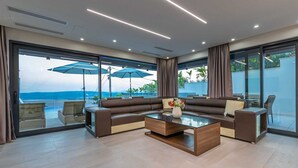 A modern living room with a sectional sofa, a glass coffee table, and large windows offering a view of the ocean.
