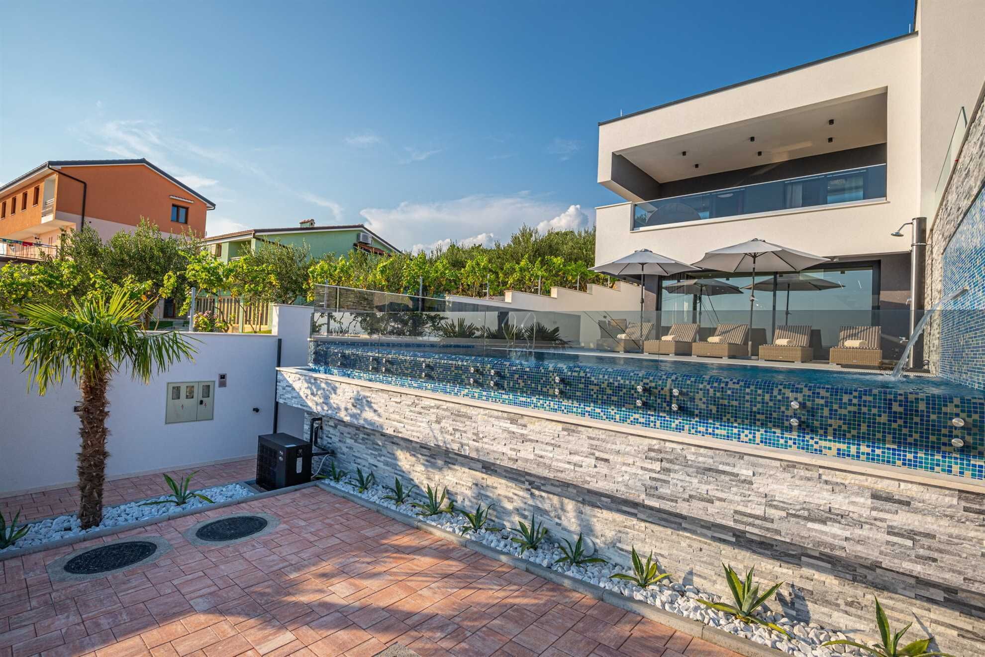 Piscina moderna al aire libre con borde de azulejos, rodeada por un muro de piedra y un patio empedrado.