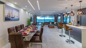 A modern dining area with a long table, multiple chairs, and a view of the sea.