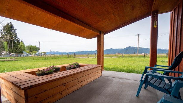 A wooden bench with potted plants, a blue chair, and a view of a grassy field and mountains. - The Cascade Mountain-View Retreat (Fort Klamath)