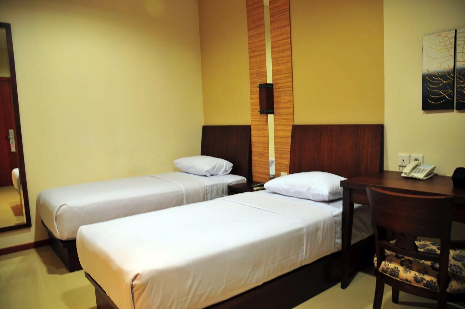 Hotellihuone, jossa on kaksi erillistä sänkyä, puinen pääty, työpöytä puhelimineen ja seinälle kiinnitetty taideteos.