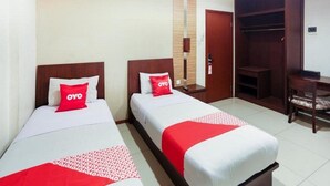 A hotel room with two beds, each with a red OYO pillow, a wooden wardrobe, and a small desk with a chair. - Thamrin Condotel (Jakarta)