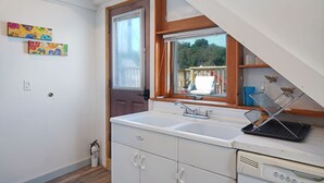 Eine Küche mit einem weißen Spülbecken, Holzschränken und einem Fenster mit Blick auf eine Terrasse.