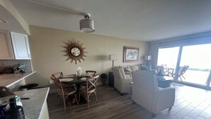 Een ruime woonkamer met een eettafel, stoelen, een bank en een groot raam met uitzicht.