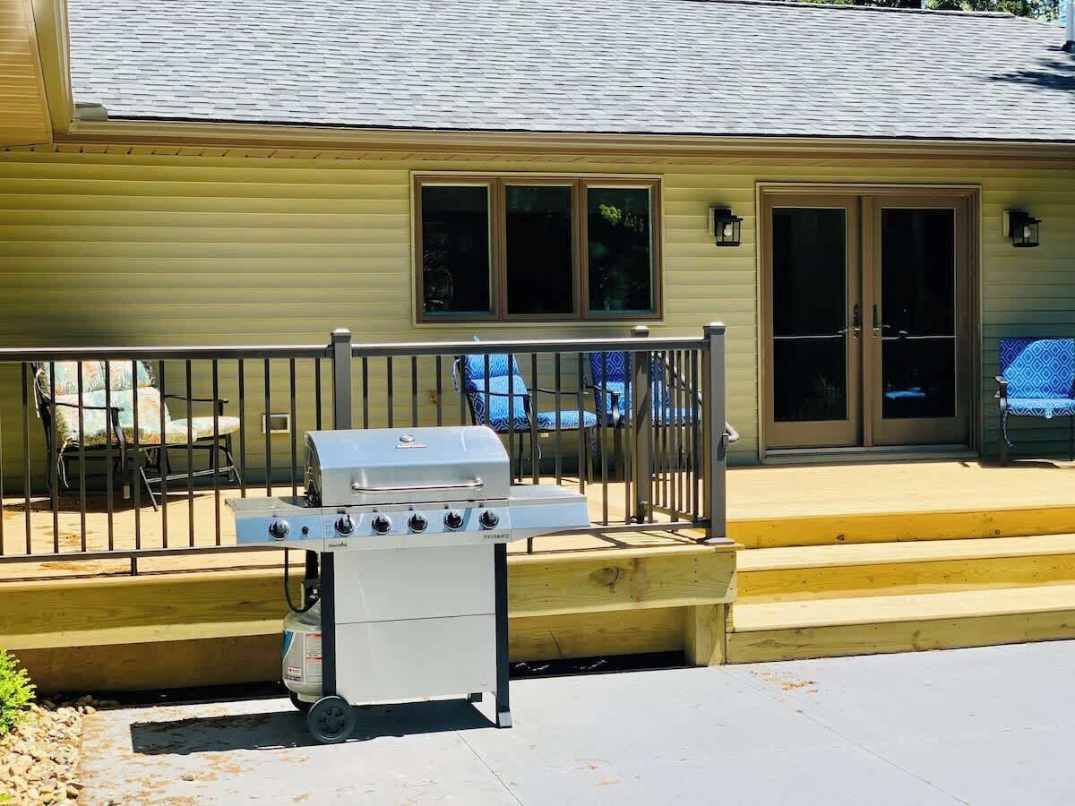 A house with a barbecue grill in front, a wooden deck, and a fenced patio area.