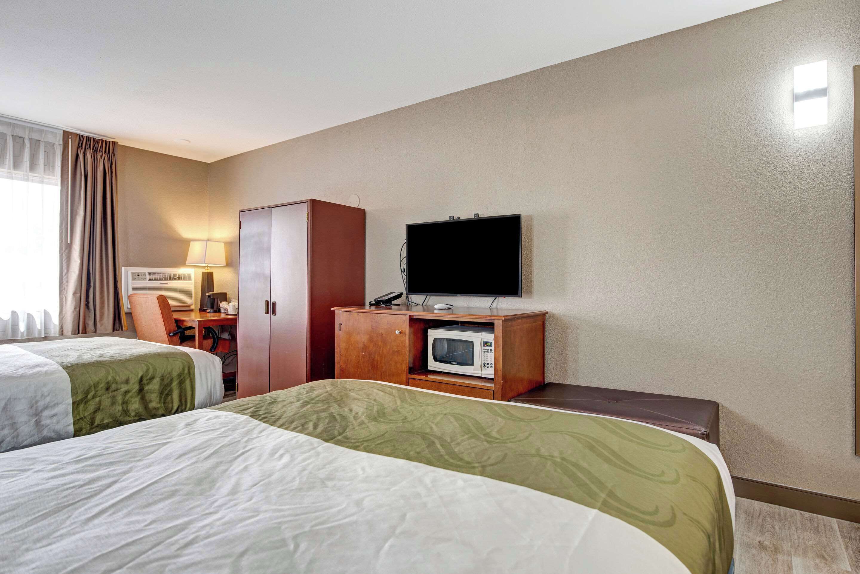 A hotel room with two beds, a desk with a chair, a television, and a microwave.
