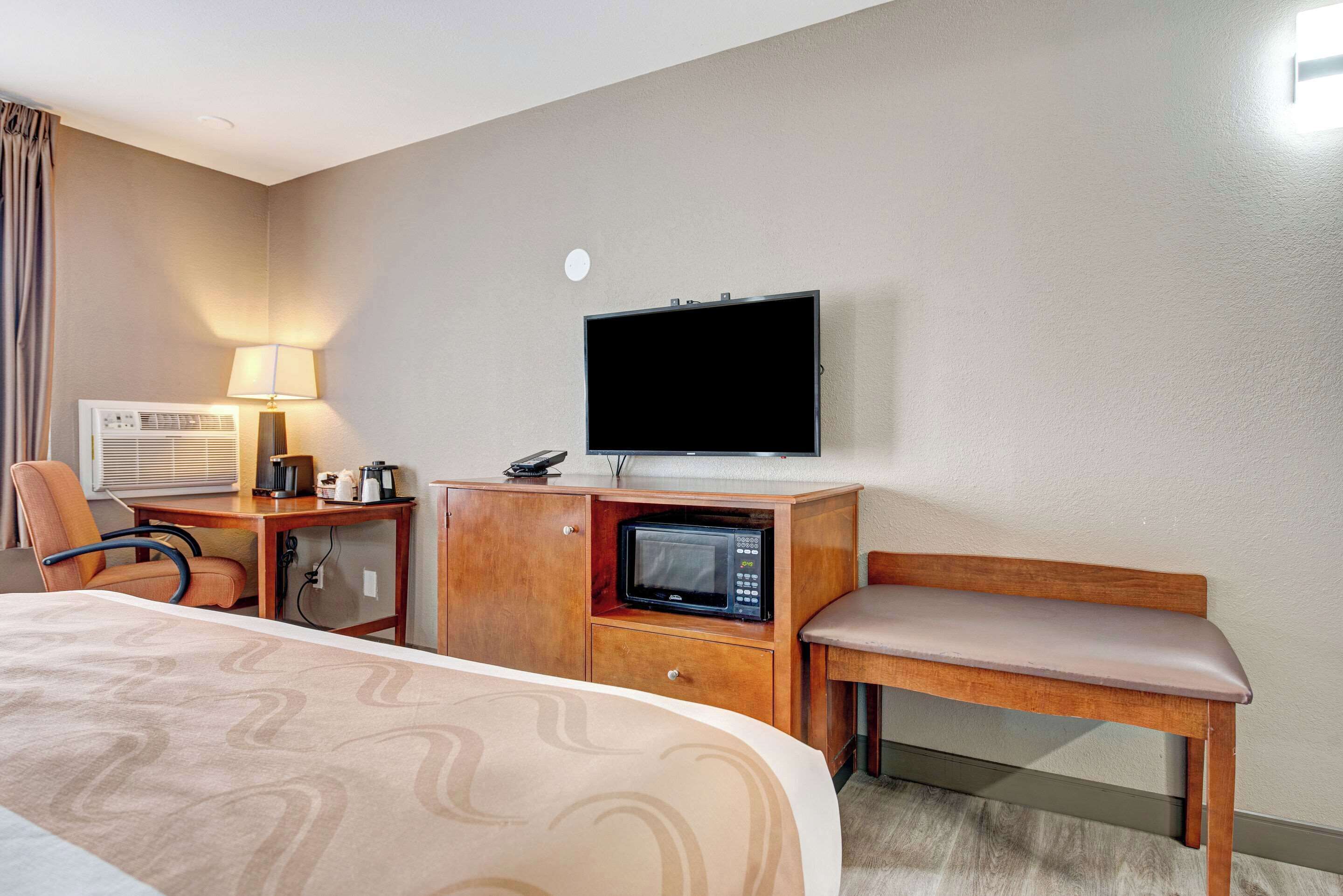 A hotel room with a bed, a desk with a lamp, a microwave, a television, and a chair.