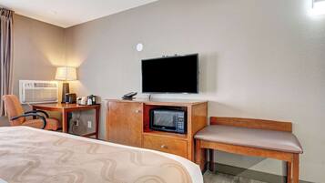 A hotel room with a bed, a desk with a lamp, a microwave, a television, and a chair.