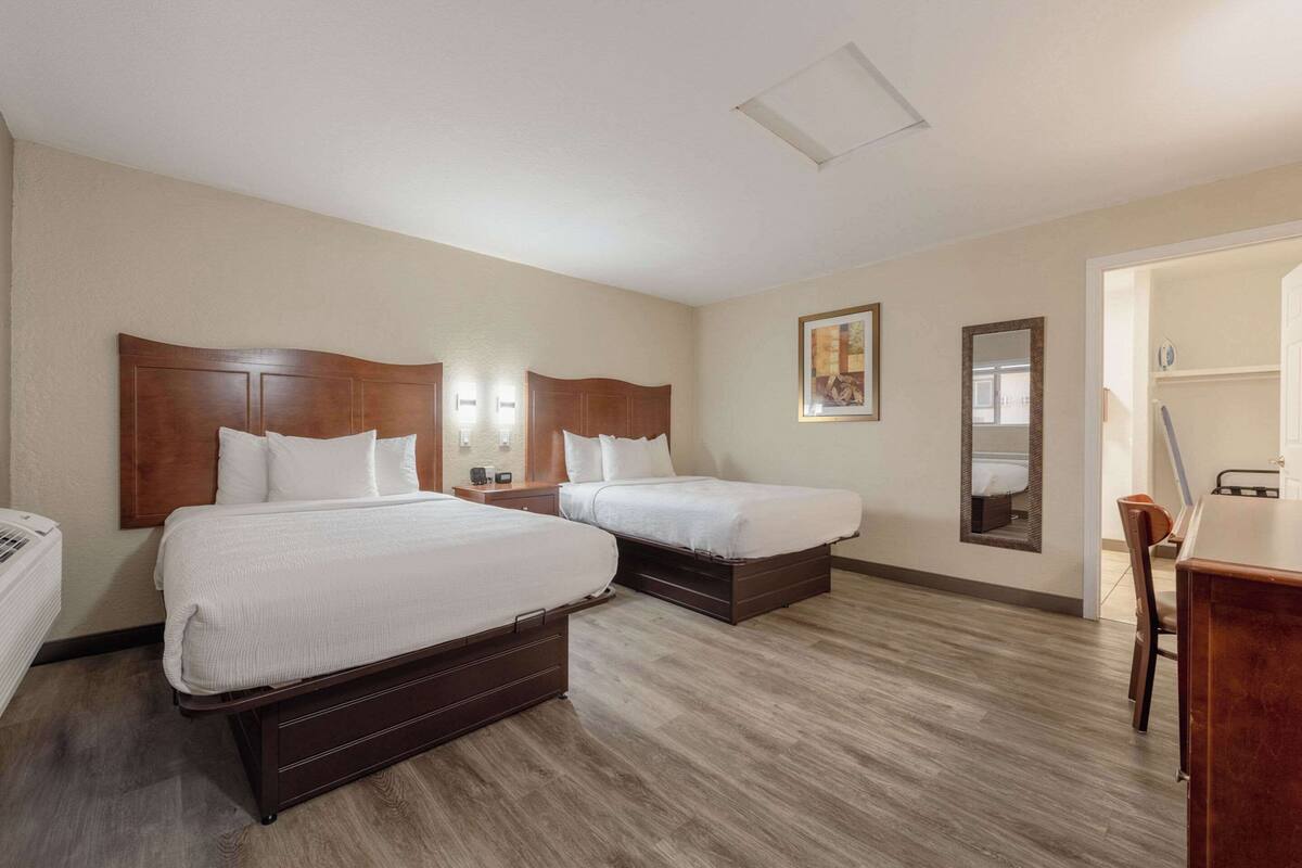 A hotel room with two beds, a desk, a chair, a mirror, and a wardrobe.
