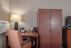 Habitación de hotel con escritorio, silla, lámpara, aire acondicionado, minibar y armario.