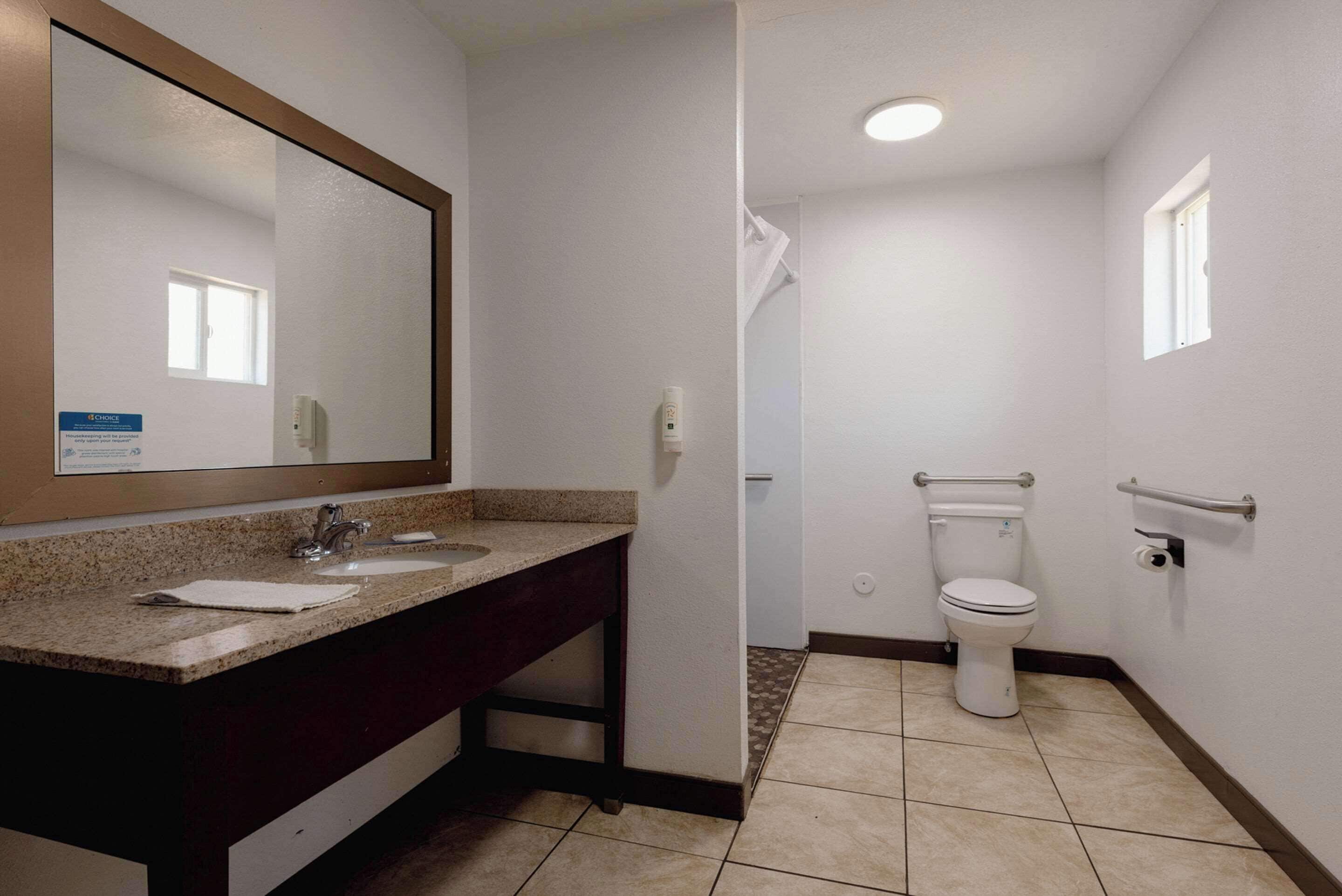 Een badkamer met een wastafel, spiegel, toilet en handgrepen.