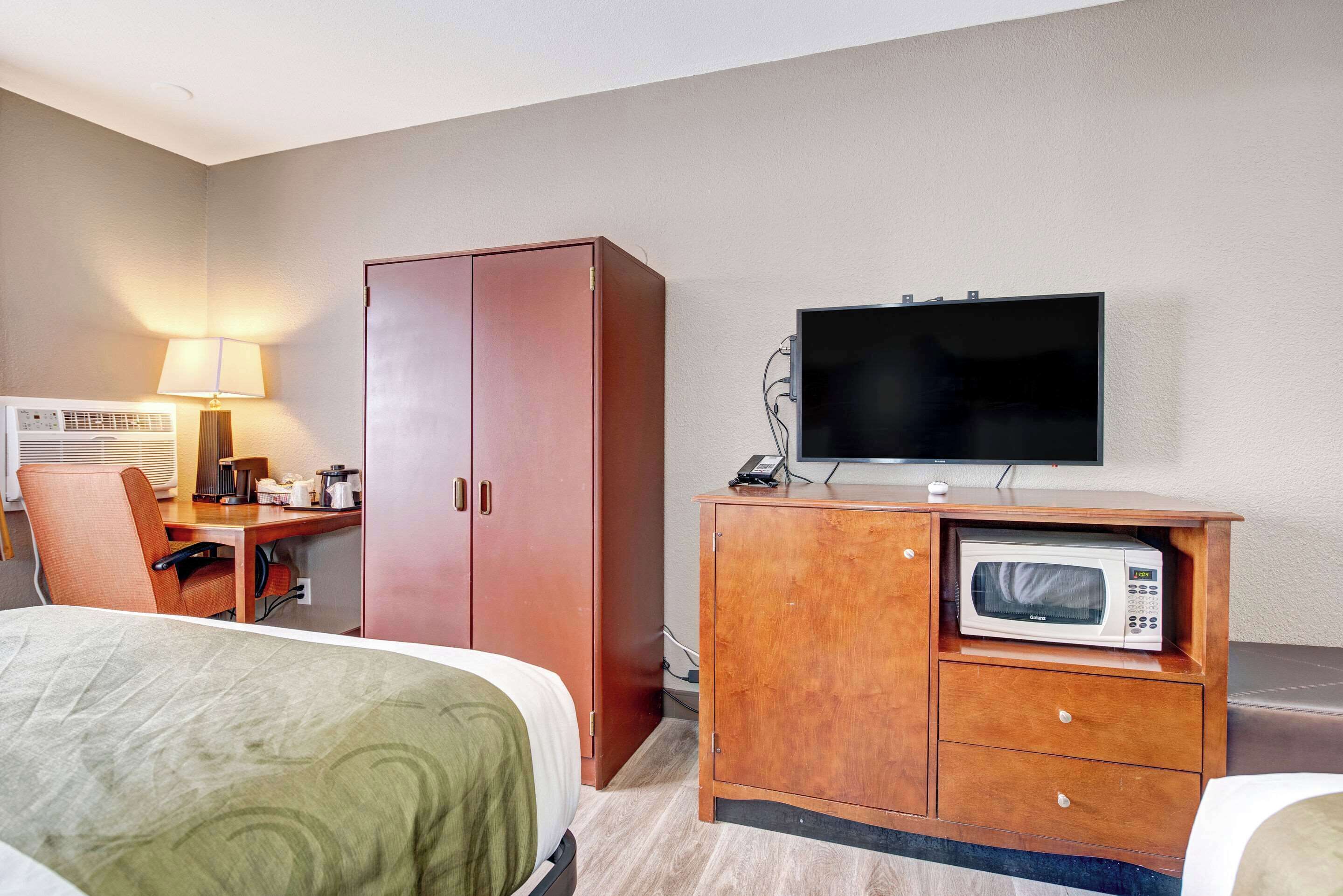 A hotel room with a bed, a desk with a lamp, a television, and a microwave.