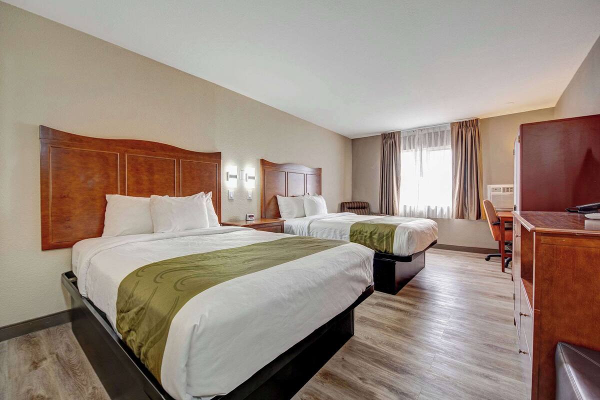 A hotel room with two beds, a desk, and a chair.
