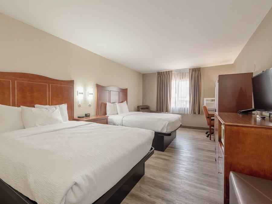 A hotel room with two beds, a desk, a television, and a window with curtains.