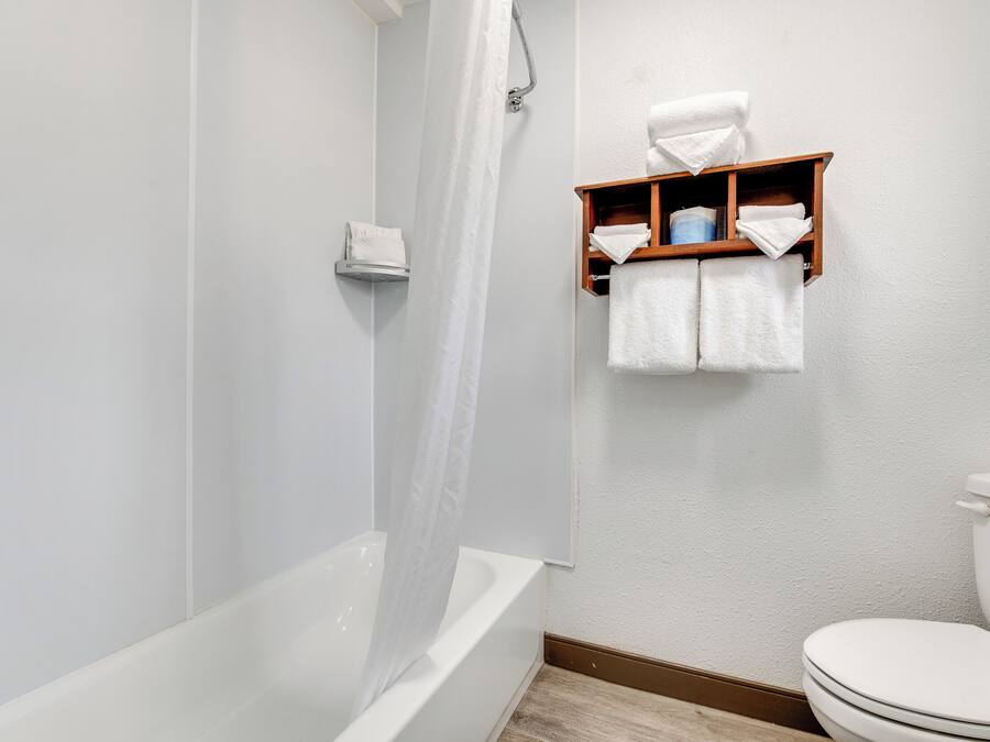 A bathroom with a bathtub, a shower curtain, a toilet, and a towel rack with towels.