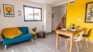 A living room with a blue sofa, a dining table with chairs, a staircase, and a yellow wall.