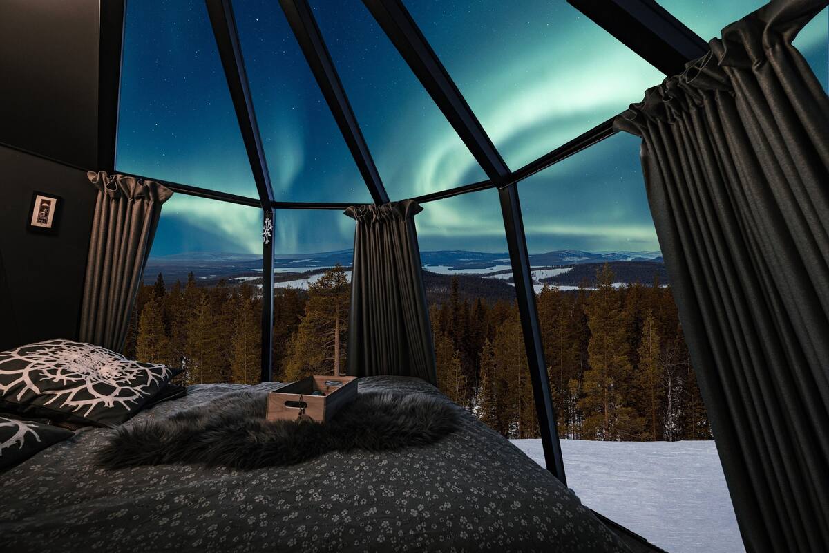Une chambre avec un lit, une petite table et une vue sur les aurores boréales.
