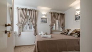 Un dormitorio con cama, cortinas, una ventana, un cuadro en la pared y una puerta.