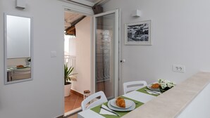 Un comedor con una mesa dispuesta para dos, una planta en maceta y un cuadro en la pared.